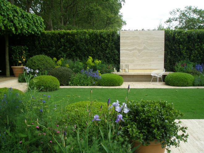 The Daily Telegraph Garden, at the 2014  Chelsea Flower Show. This is just a portion of the elegant space designed by Tommaso del Buono and Paul Gazerwitz. Tommaso grew up in Florence, and Paul in New York, and together they have an international practice, based in Shoreditch, East London. Here, a giant panel of Nocino Travertine Limestone punctuates a tall, green hedge. Low topiaries, pruned into pincushion shapes, flank a bench that floats in front of the limestone.